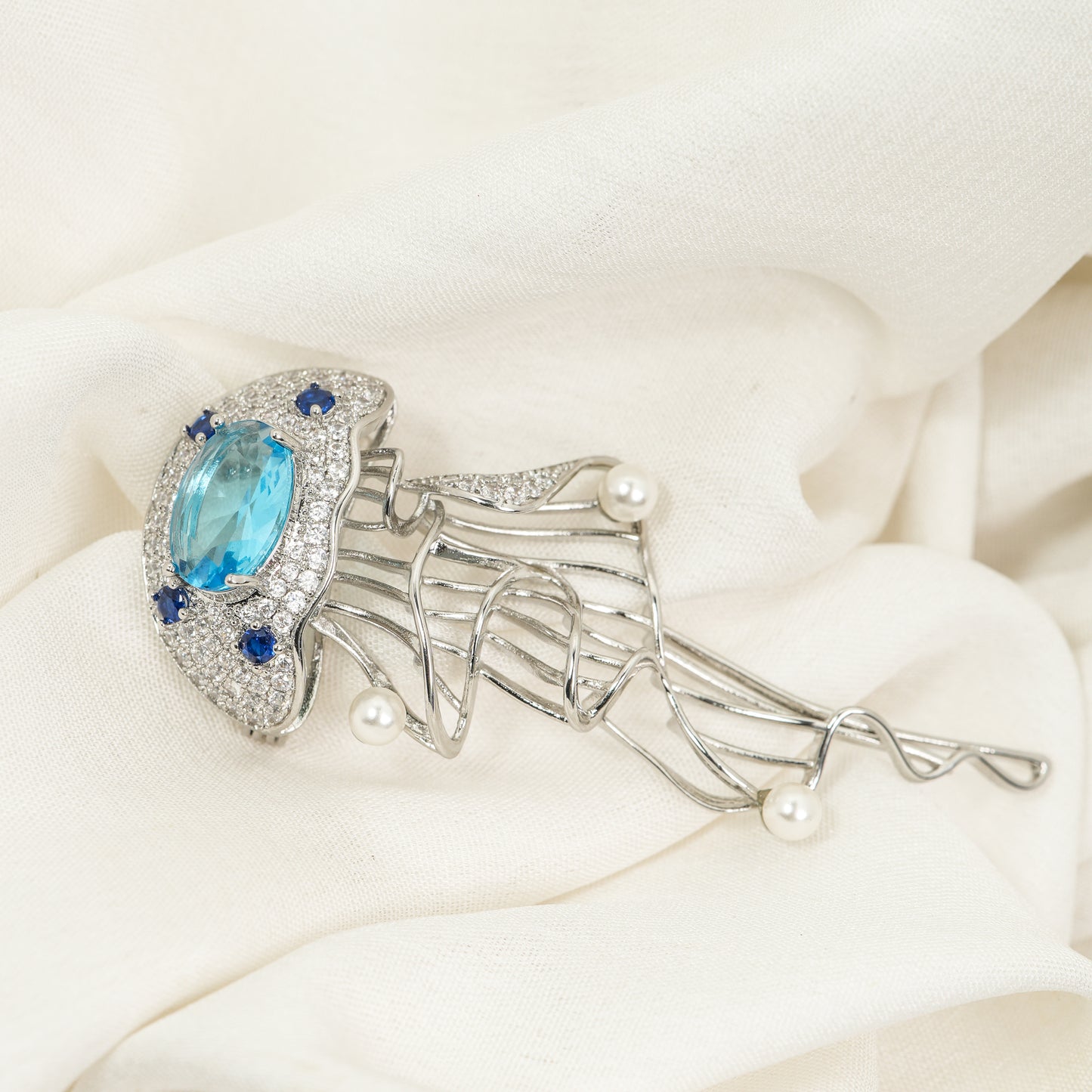 Aquatic Art Pave Brooch | Silver Tone Jellyfish Inspired Brooch with Aquamarine Coloured Center Stone, Blue CZ Accents, Flowing Metal Lines and Pearl Details | Unique Artistic Statement Pin